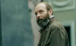 Mężczyzna z brodą, niczym geist lalka, spogląda przez ramię w brązowej marynarce.