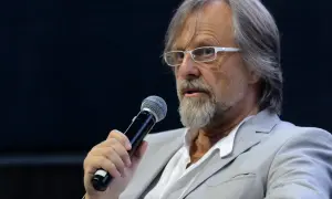 Mężczyzna w okularach i jasnej marynarce trzyma mikrofon. Człowiekiem jestem i nic co ludzkie nie jest mi obce, nawet gdy przemawiam do tłumu.