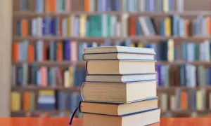 Stos książek na biurku, tło biblioteki z kolorowymi grzbietami. Idealne lektury na e8.