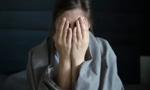Kasandra ukrywa twarz w dłoniach, otulona kocem, jakby chciała zniknąć.