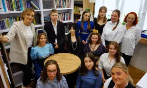 Grupa osób w strojach historycznych, jakby z powieści Dostojewskiego, pozuje na tle regałów z książkami.