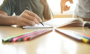 Uczeń pisze, opierając się na empiryzmie i doświadczeniu, z kolorowymi kredkami i otwartą księgą.