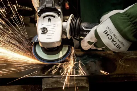 Ręka w rękawicy Hitachi szlifuje metal, tworząc deszcz iskier. To przykład działania siły tarcia statycznego.