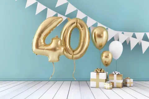 Złote balony z cyfrą 40, prezenty i girlanda z chorągiewek tworzą dekorację na 40 urodziny.