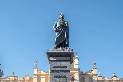 Pomnik Adama Mickiewicza, symbol romantyczności, na tle błękitnego nieba i zabytkowych kamienic.