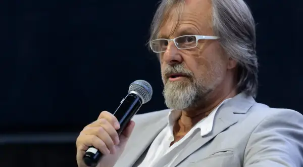 Mężczyzna w okularach i jasnej marynarce trzyma mikrofon. Człowiekiem jestem i nic co ludzkie nie jest mi obce, nawet gdy przemawiam do tłumu.