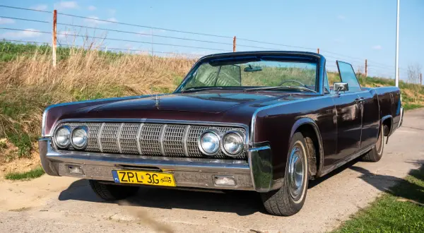 Klasyczny Lincoln w kolorze śliwkowym, kabriolet, z chromowanymi detalami i żółtą tablicą rejestracyjną, stoi na drodze.