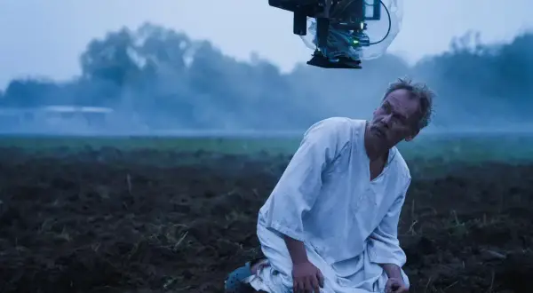Syn Macieja Boryny klęczy na zaoranym polu. Nad nim wisi kamera filmowa.