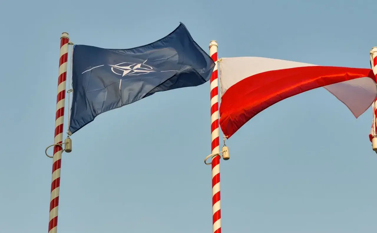 Flaga NATO i biało-czerwona flaga Polski powiewają na tle błękitnego nieba. Dwa państwa NATO razem.