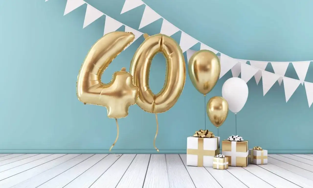 Złote balony z cyfrą 40, prezenty i girlanda z chorągiewek tworzą dekorację na 40 urodziny.