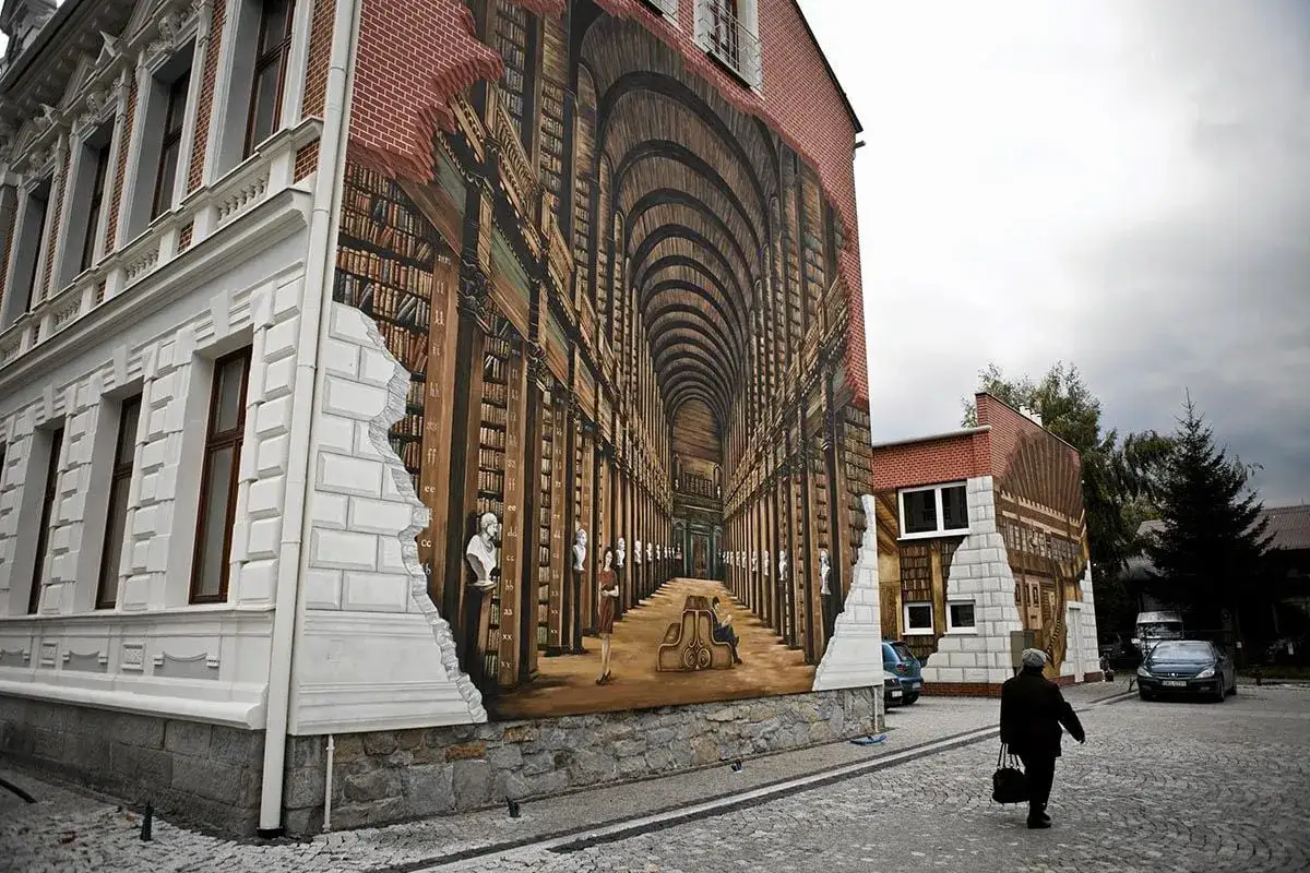 Mural na ścianie budynku przedstawia iluzję biblioteki, gdzie motyw miasta w literaturze ożywa wśród regałów pełnych książek.