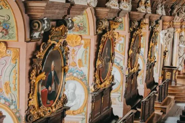 Wnętrze z portretami w złotych ramach, ozdobnymi malowidłami i rzeźbami. Idealizm epoki widoczny w kunsztownych detalach.