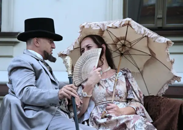 Para z epoki, mężczyzna w cylindrze i eleganckim garniturze, kobieta z wachlarzem i parasolką. Ich stylizacja to lalka opracowanie.