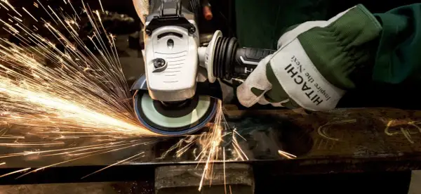 Ręka w rękawicy Hitachi szlifuje metal, tworząc deszcz iskier. To przykład działania siły tarcia statycznego.