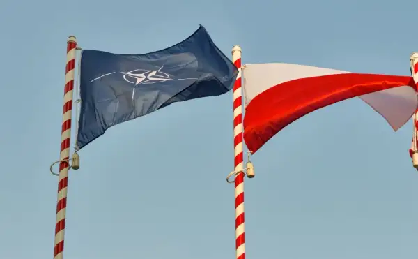 Flaga NATO i biało-czerwona flaga Polski powiewają na tle błękitnego nieba. Dwa państwa NATO razem.